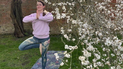 A yoga teacher doing a tree yoga pose on a yoga mat underneath a blossom tree in the orchard